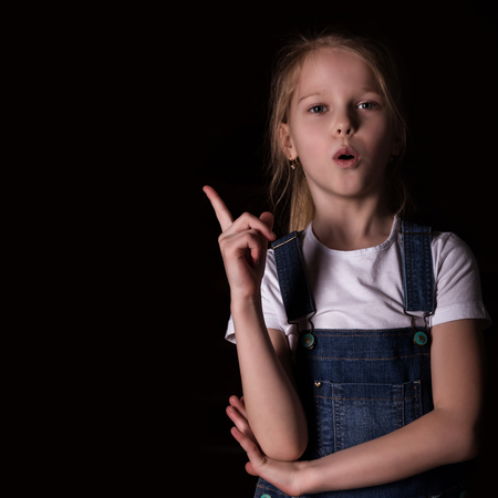 beautiful blonde little girl on a dark background. She stands in different poses and shows different emotions. free space for your textの写真素材