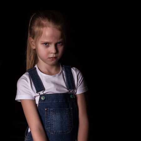 beautiful blonde little girl on a dark background. She stands in different poses and shows different emotions. free space for your textの写真素材