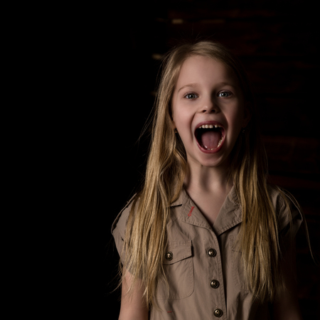 beautiful blonde little girl on a dark background. She stands in different poses and shows different emotions. free space for your textの写真素材