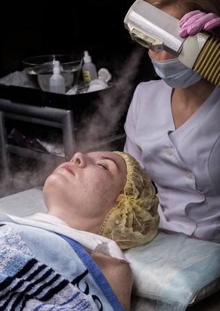 Doctor cleanses the womans skin with a steam. young woman with problem skin at the beautician. Cosmetology conceptの写真素材
