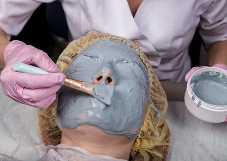 Cosmetologist applying facial mask to problem skin. young woman having face cleaning procedureの写真素材
