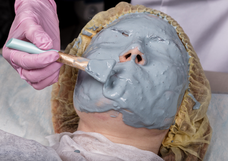 Cosmetologist applying facial mask to problem skin. young woman having face cleaning procedureの写真素材