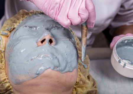 Cosmetologist applying facial mask to problem skin. young woman having face cleaning procedureの写真素材