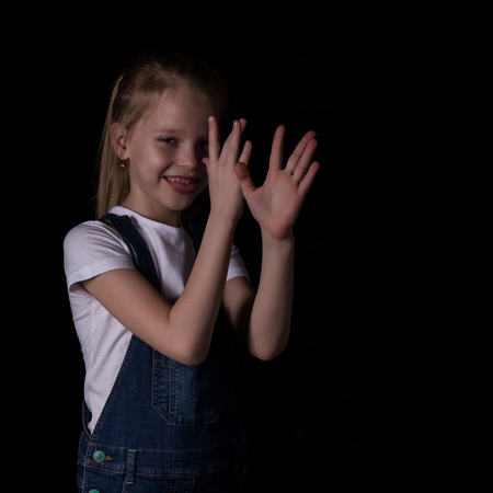 beautiful blonde little girl on a dark background. She stands in different poses and shows different emotions. free space for your textの写真素材