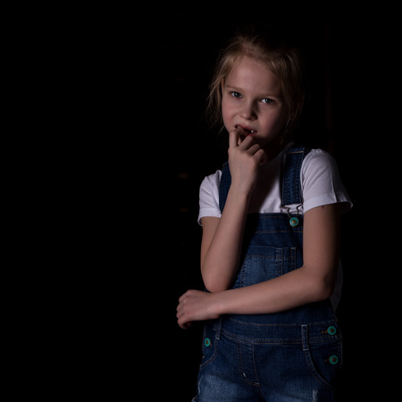 beautiful blonde little girl on a dark background. She stands in different poses and shows different emotions. free space for your textの写真素材