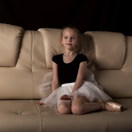 little ballerina in pointe sits and resting on the sofa. cute ballerina in the dance class is studying ballet. Classical dance, balletの写真素材