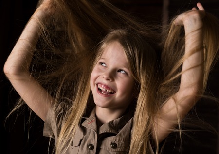 funny lovely little blonde child with different emotions on a dark background. beautiful schoolgirl holding herself hairの写真素材