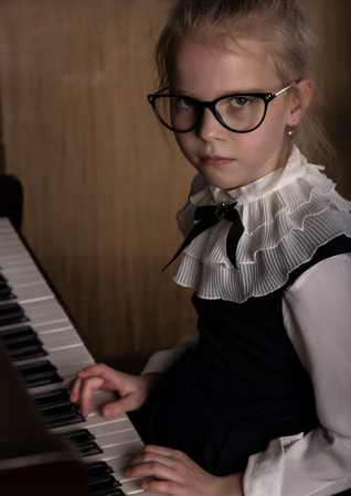 strict little girl in a big glasses playing the piano, child imitates teacherの写真素材