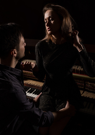 young woman with sexy body legs and buttocks sitting on a old wooden piano opposite the handsome guyの写真素材