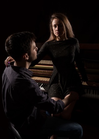 young woman with sexy body legs and buttocks sitting on a old wooden piano opposite the handsome guyの写真素材