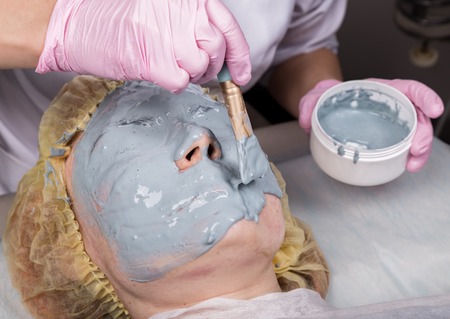 Cosmetologist applying facial mask to problem skin. young woman having face cleaning procedureの写真素材