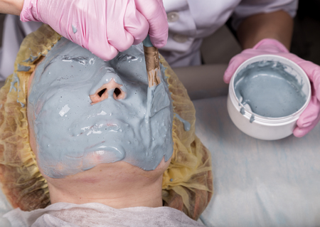 Cosmetologist applying facial mask to problem skin. young woman having face cleaning procedureの写真素材