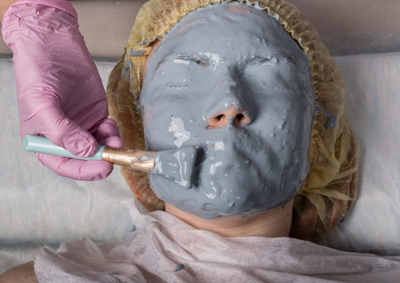 Cosmetologist applying facial mask to problem skin. young woman having face cleaning procedureの写真素材