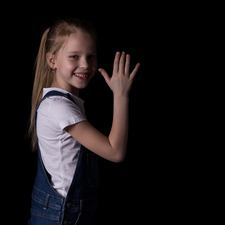 beautiful blonde little girl on a dark background. She stands in different poses and shows different emotions. free space for your textの写真素材