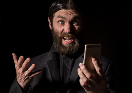 Old believer senior priest with a smartphone, bearded old man is calling on a dark backgroundの写真素材