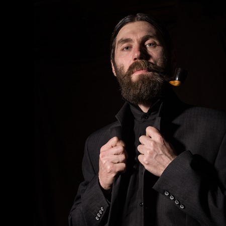 vintage handsome bearded man with a smoking pipe on a dark background. free space for your textの写真素材