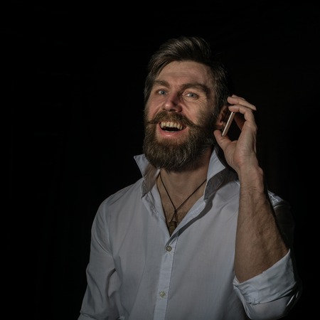 handsome bearded man using his phone with smile on a dark backgroundの写真素材