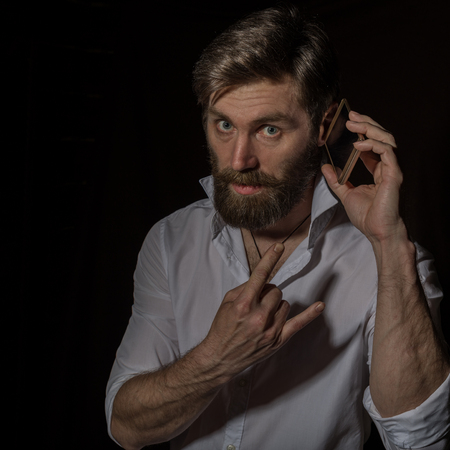 handsome bearded man using his phone with smile on a dark backgroundの写真素材
