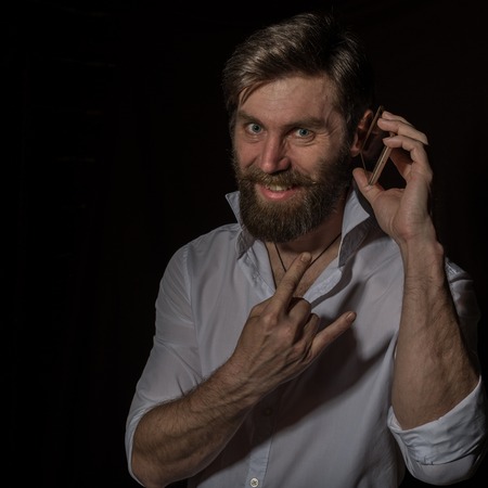 handsome bearded man using his phone with smile on a dark backgroundの写真素材