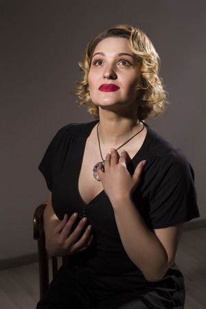 Retro portrait of beautiful woman in black dress sitting on the chair on gray background. Vintage styleの写真素材
