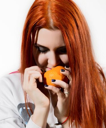 young redhead woman eats citrus orange fruit having funの写真素材