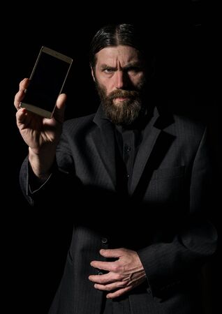 Old believer senior priest with a smartphone, bearded old man is calling on a dark backgroundの写真素材