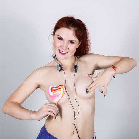 Young sexy redhead woman with headphones licks heart shaped lollipopの写真素材