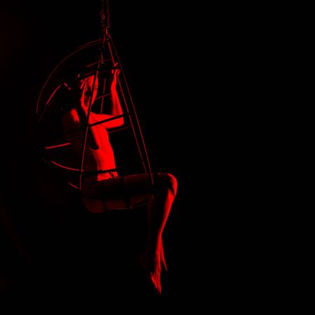 silhouette of sexy woman in red light on a dark background. leggy woman in a bodysuit with metal rings. free space for textの写真素材