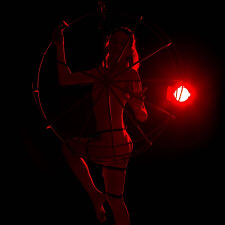 silhouette of sexy woman in red light on a dark background. leggy woman in a bodysuit with metal ringsの写真素材