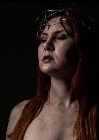 tormented beautiful woman with a wreath of barbed wire on the head on a dark backgroundの写真素材