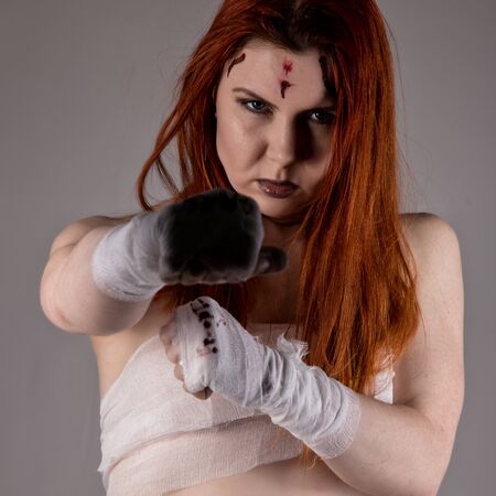 young redhead female fighter after the fight in a dark. girls in martial arts. bloody bandages with fistsの写真素材