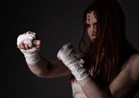 young redhead female fighter after the fight in a dark. girls in martial arts. bloody bandages with fistsの写真素材