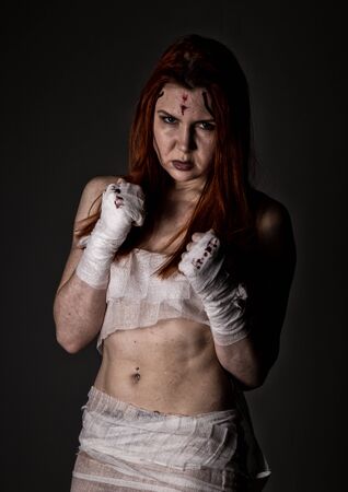 young redhead female fighter after the fight in a dark. girls in martial arts. bloody bandages with fistsの写真素材