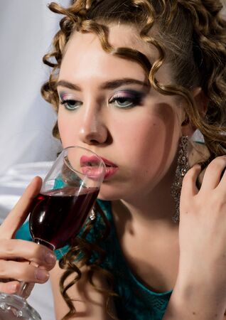 beautyful young curly woman resting on the bed in a hotel room and enjoying red wineの写真素材