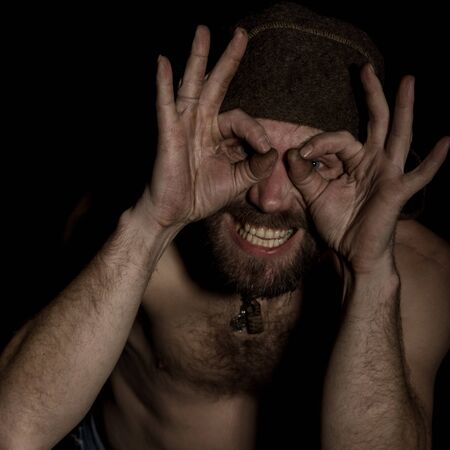 strange Russian man with a naked torso and a woolen hat doing different signs with her handsの写真素材