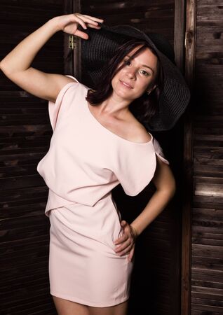 Fashionable woman posing in wide-brimmed black hat. Woman in elegant outfit. Woman fashionable brunette stands on a wooden background.の写真素材