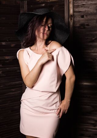 Fashionable woman posing in wide-brimmed black hat. Woman in elegant outfit. Woman fashionable brunette stands on a wooden background.の写真素材