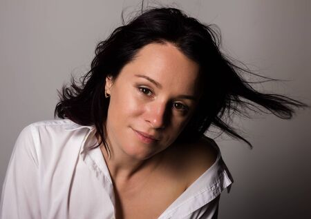 Fashionable woman in a mans white shirt with bare shoulder on a gray backgroundの写真素材
