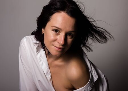 Fashionable woman in a mans white shirt with bare shoulder on a gray backgroundの写真素材