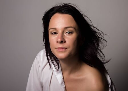 Fashionable woman in a mans white shirt with bare shoulder on a gray backgroundの写真素材