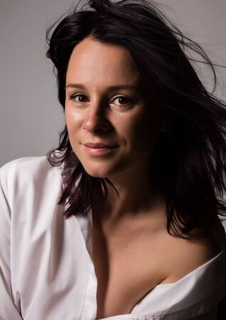 Fashionable woman in a mans white shirt with bare shoulder on a gray backgroundの写真素材