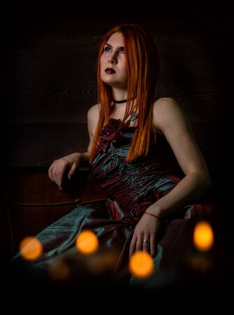redhaired woman in a retro dress with candles on black backgroundの写真素材