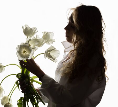 silhouette of beautiful curly girl with spring flowers tulips on a white backgroundの写真素材