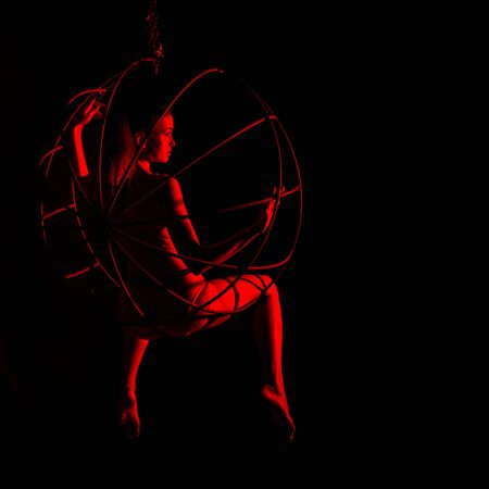 silhouette of sexy female dancer in red light on a dark background. leggy woman in a bodysuit with metal rings. night club concepteの写真素材