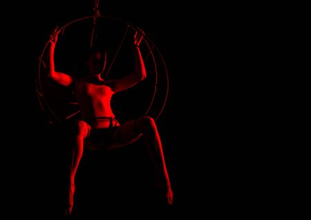 silhouette of sexy female dancer in red light on a dark background. leggy woman in a bodysuit with metal rings. night club concepteの写真素材
