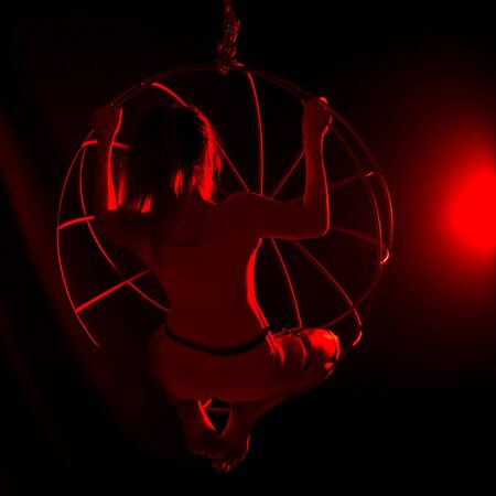 silhouette of sexy female dancer in red light on a dark background. leggy woman in a bodysuit with metal rings. night club concepteの写真素材