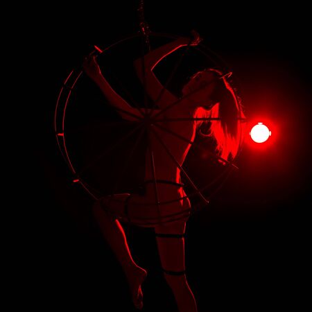 silhouette of sexy woman in red light on a dark background. leggy woman in a bodysuit with metal ringsの写真素材