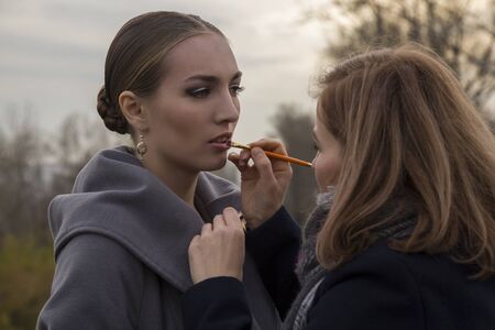 makeup artist makes make up for beautiful model outdoor. paints lips with a brushの写真素材