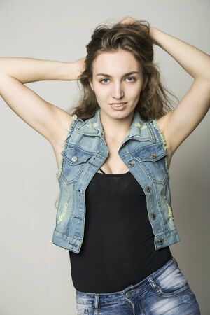 young beautiful happy stylish hipster girl in a denim jacket and shorts posing on a light backgroundの写真素材