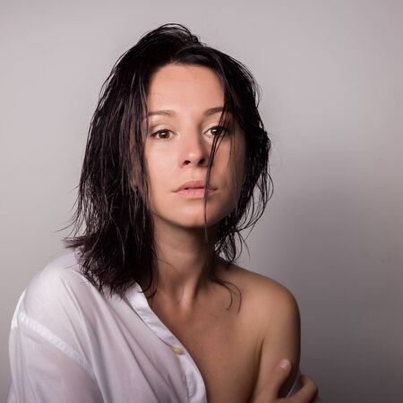 Fashionable woman in a mans white shirt with bare shoulder on a gray backgroundの写真素材